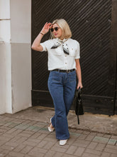 A lady wears a knitted cardigan and bootcut jeans.